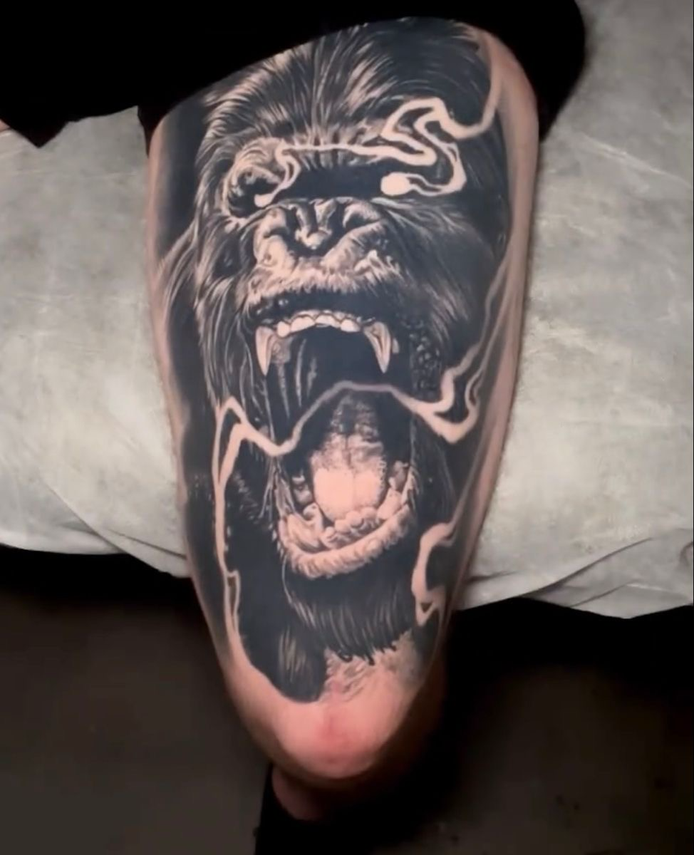 Black and grey realism tattoo of a roaring gorilla with electrical arcs on a thigh